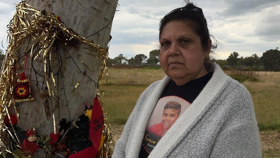 Mechelle Turvey stands next to a memorial wall