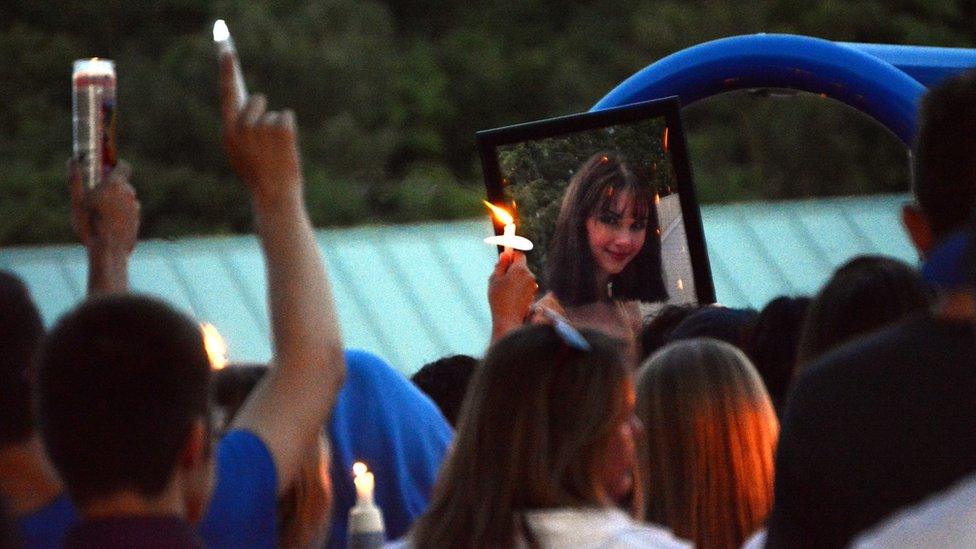 A photograph of Bianca is held at a vigil, where candles are seen in the air