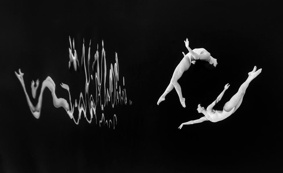 Synchronised swimmers pose for an underwater portrait in front of a black background