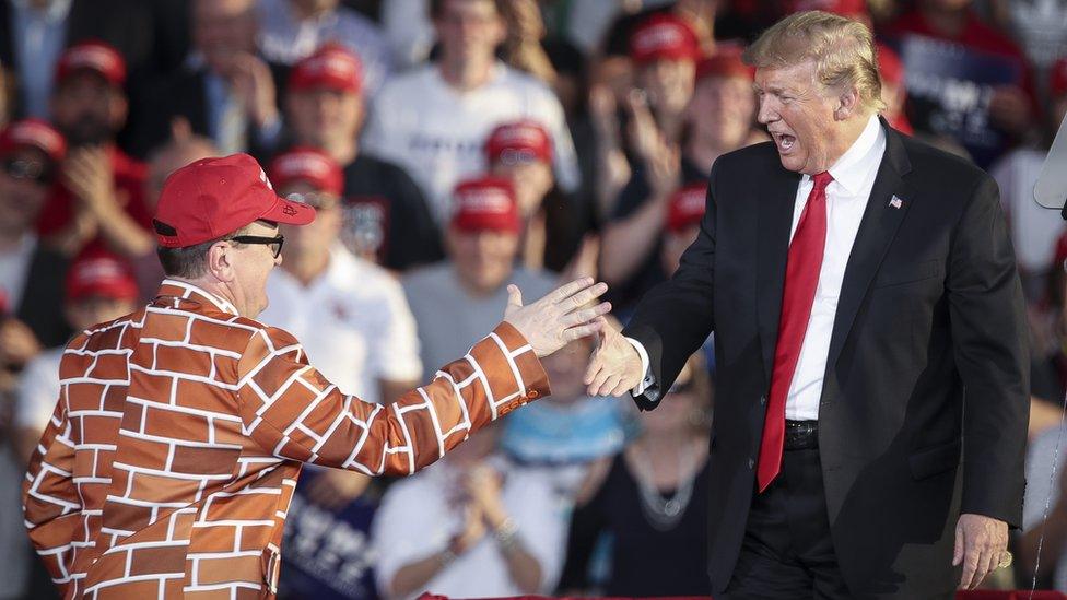 Trump greets a man dressed in a border wall suit during a rally