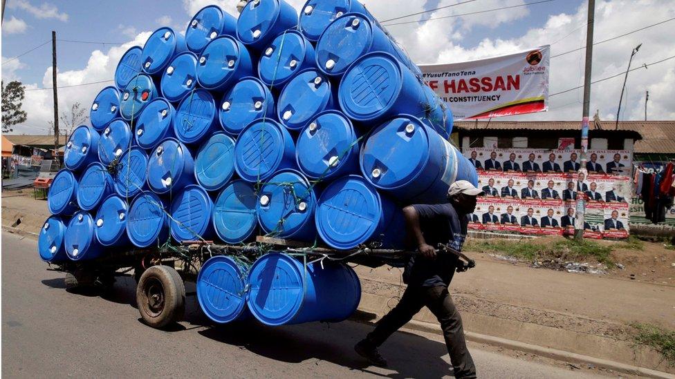 A porter transports a cart loaded with empty plastic drums to a recycling dealer