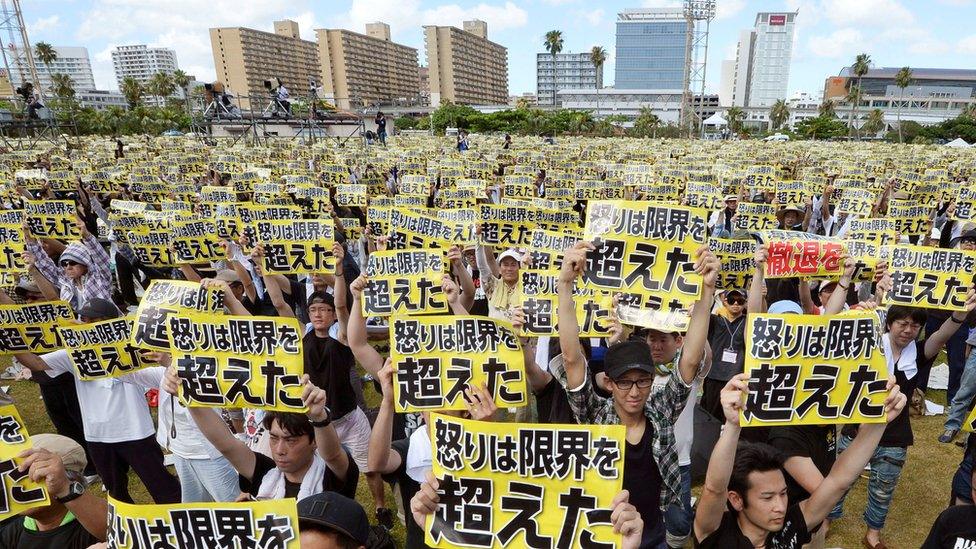 Protesters raise placards reading "Anger was over the limit" during a rally against the U.S. military presence on the island