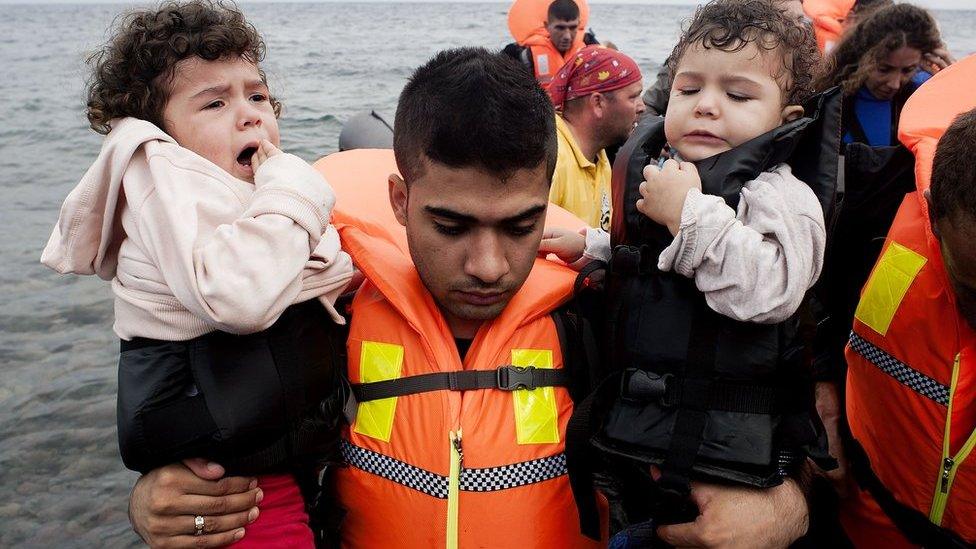 A refugee man carries children upon their arrival on Sykamia beach, west of the port of Mytilene, on the Greek island of Lesbos after crossing the Aegean sea from Turkey on September 22, 2015.