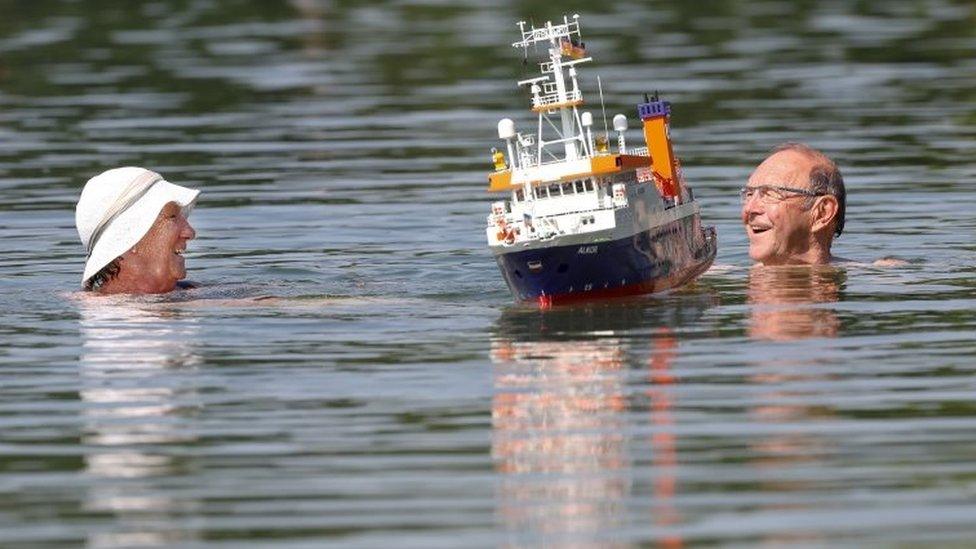 A couple swim past a model boat at the Schwarzachtal lakes in southern Germany