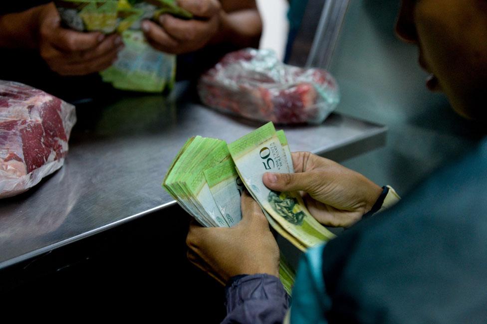 Shopper paying for meat with sheaf of banknotes