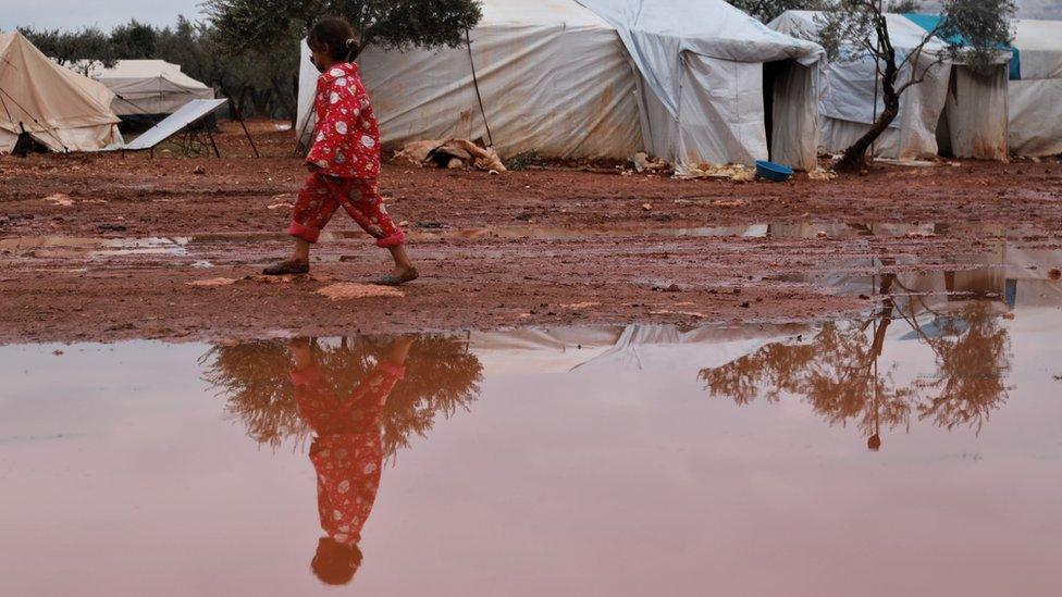 A girl walks through a flooded camp in north-western Syria