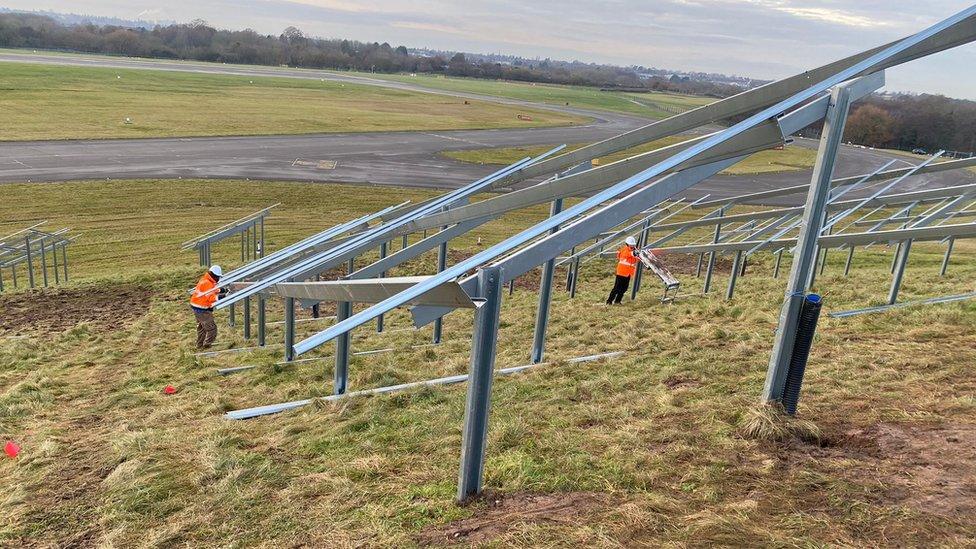 Mounting frame for solar panels standing on grass, with two students in orange hi-viz working on it