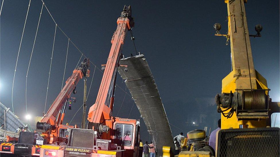 Workers remove a section of a suspension bridge (C) after the structure collapsed across the river Machchhu in Morbi, some 220 kms from Ahmedabad, early on October 31, 2022