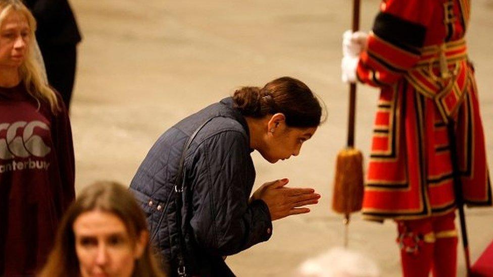 Woman with hands in praying position as she sees the Queen's coffin.