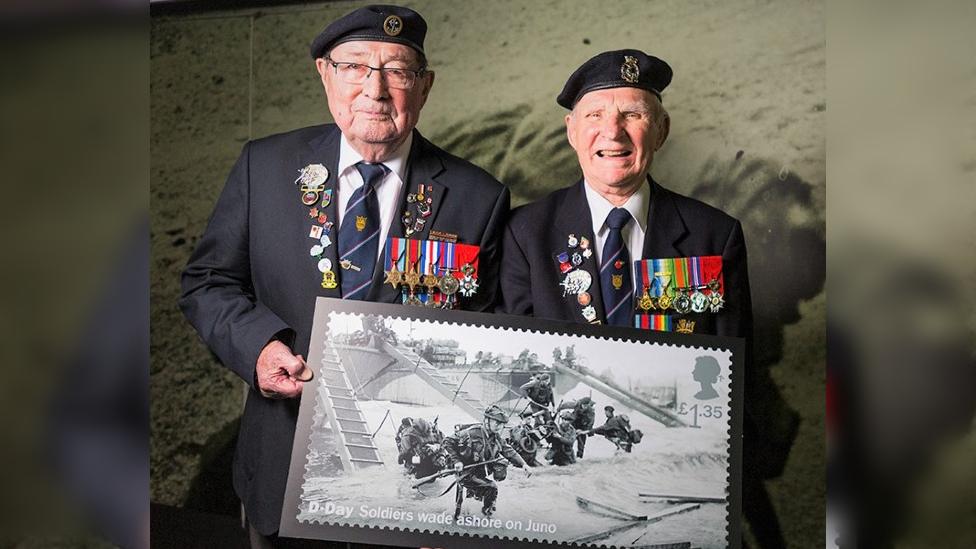 Two veterans standing with a stamp wearing medals