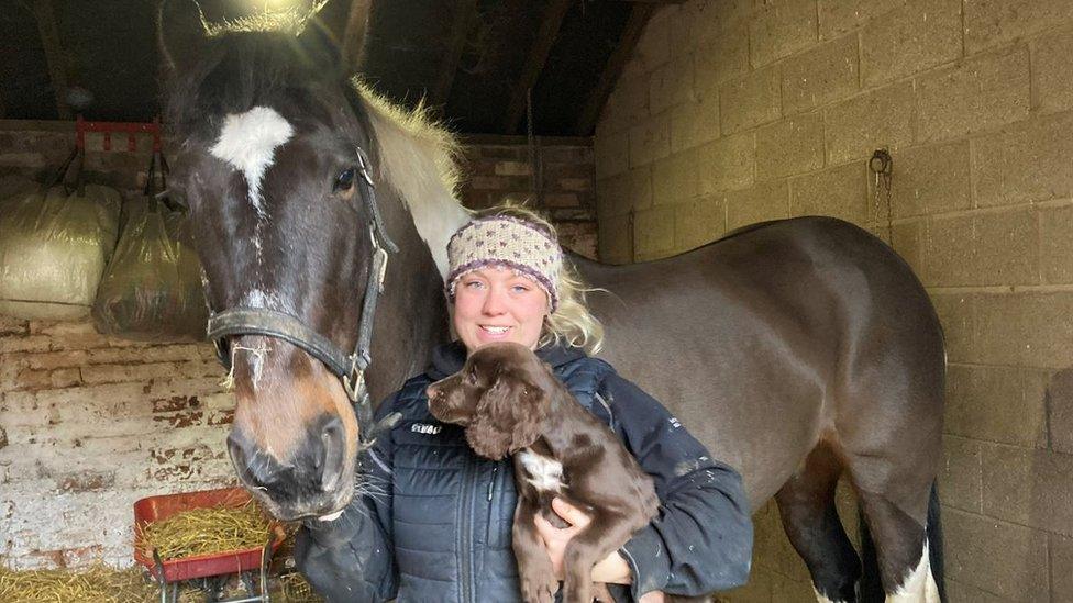 A woman holding a dog with her horse