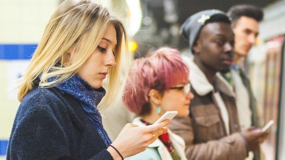 A woman looks at her phone on a tube platform in London