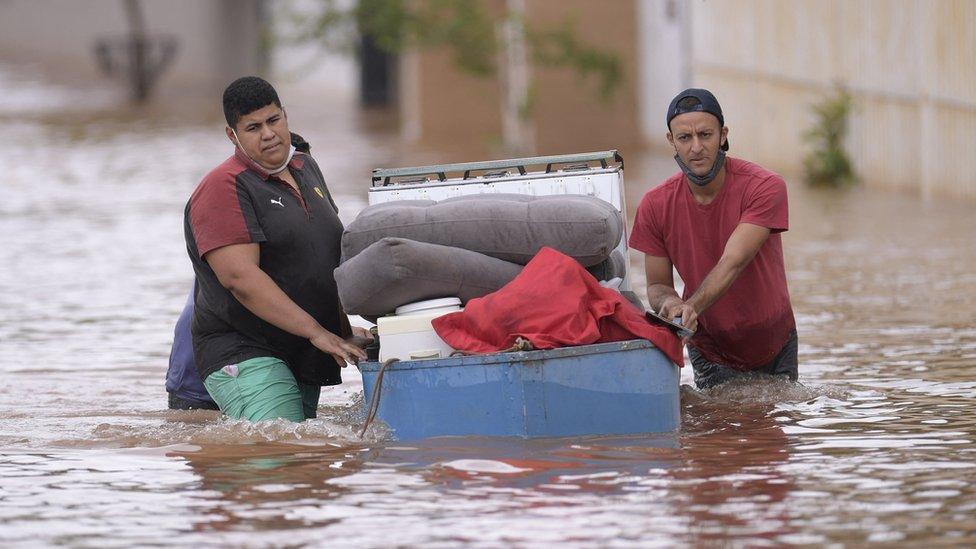 People wade through the water as they remove belongings from their homes in the flooded Brazilian municipality of Juatuba