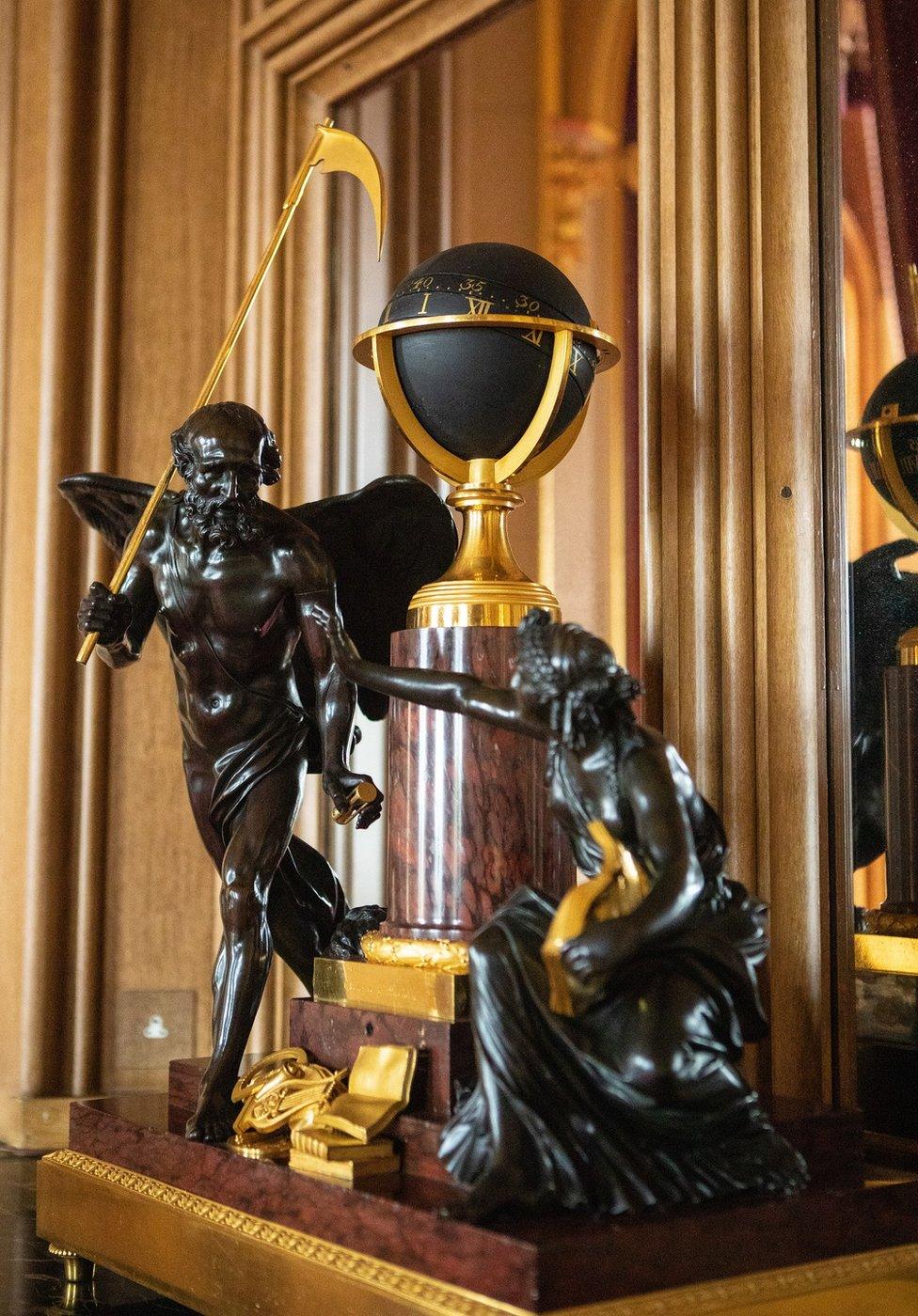 A close-up of a clock that features two bronze statues of the mythological figures of Time and Study