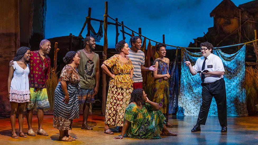 Book of Mormon musical showing Elder Cunningham preaching to Ugandan villagers