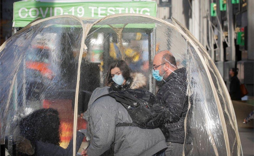 People take Covid-19 tests at a pop-up testing site in New York on 1 December. They are wearing masks and can be seen inside a transparent tent