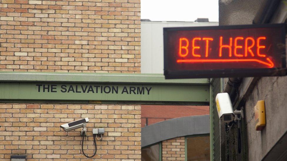 An alley with a neon sign saying 'Bet Here' next to a Salvation Army sign