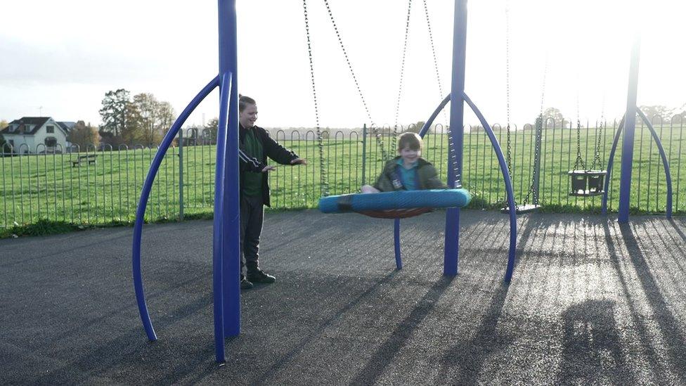 Reggie pushing Eli on a swing in the playground