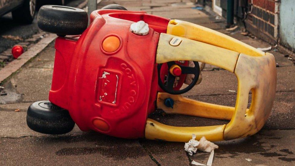 Yellow and red "little tikes" car on its side on a pavement