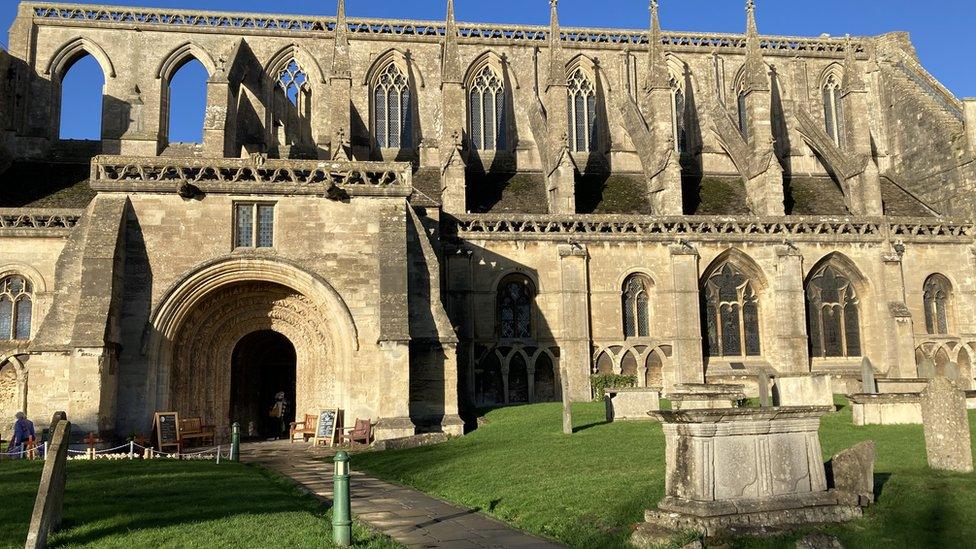 Malmesbury Abbey under a bright blue sky with churchyard in front.