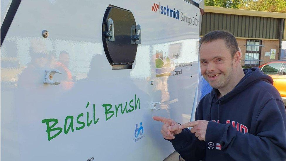 Side of a street sweeper bearing the legend "Basil Brush". A young man in a blue top is pointing to the name.