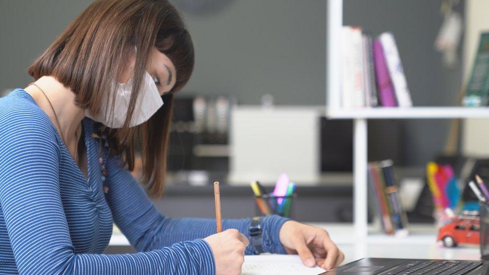 A young woman studying in a library while wearing a mask