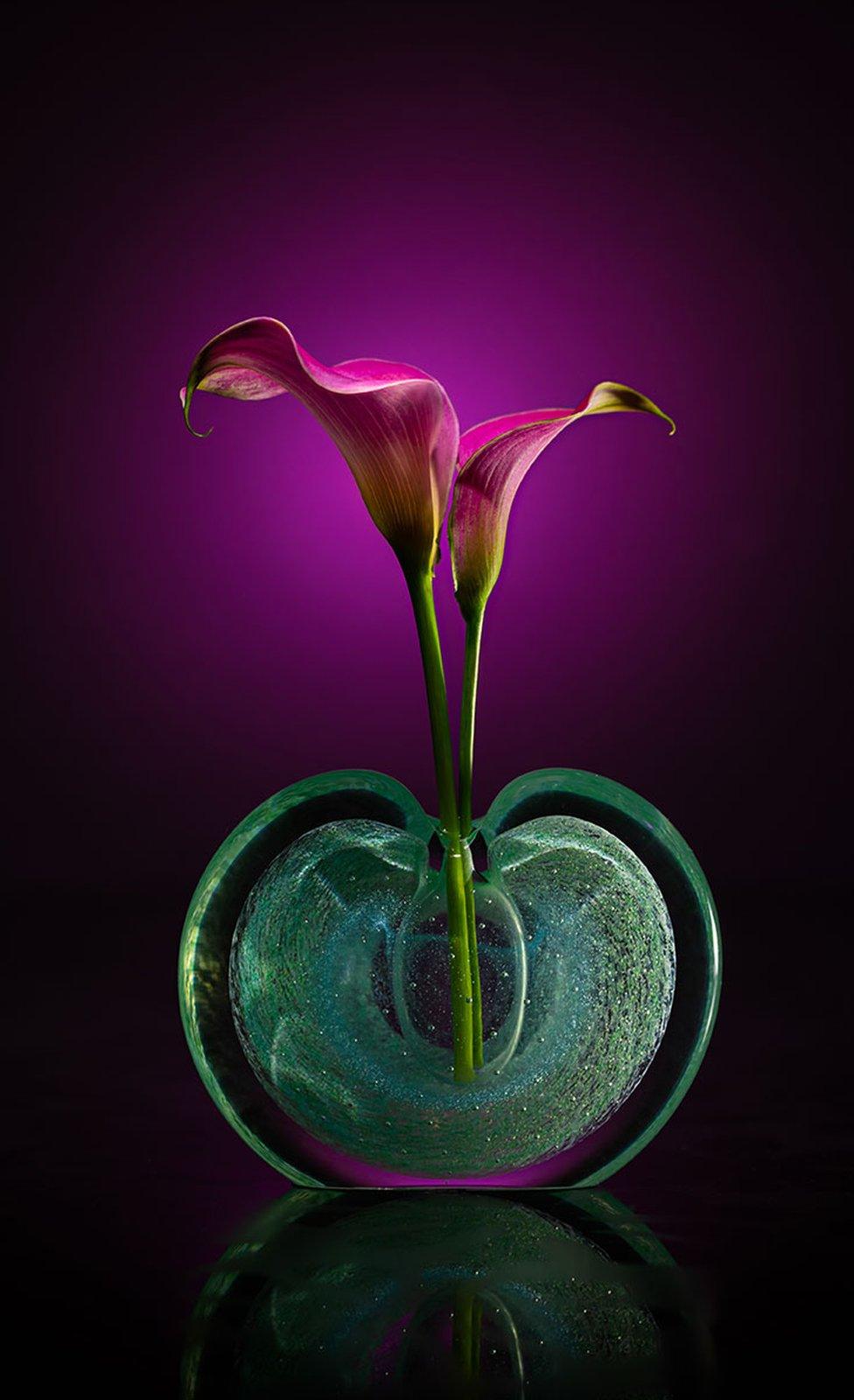 Two flowers in a perfume bottle with a dark purple background