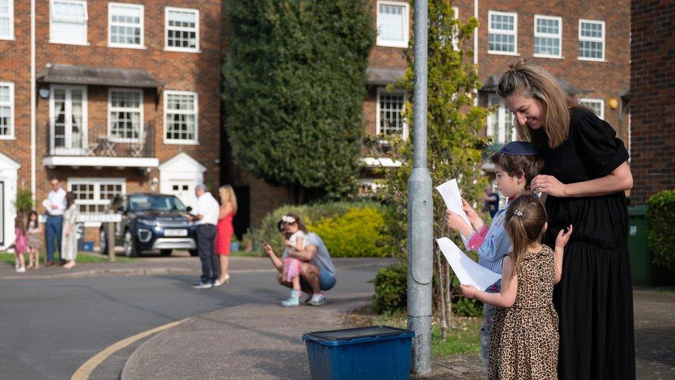 Residents socially distance as they stand outside their homes to sing ahead of the beginning of Passover