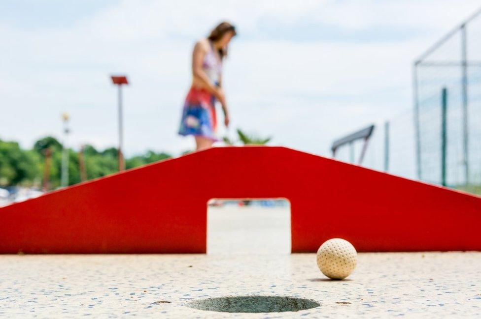 Woman playing mini-golf through a novelty tunnel