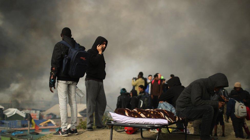 Some migrants still roaming the Calais camp as smoke billows during a fire incident on 26 October, 2016.