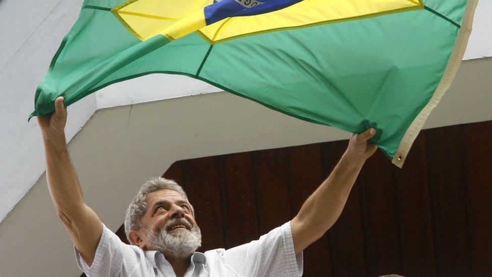 Luiz Inacio Lula da Silva waves a Brazilian flag to supporters from the balcony of his apartment