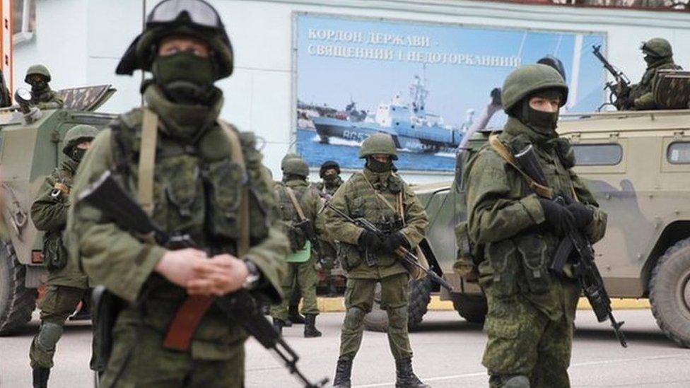 Armed servicemen wait near Russian army vehicles outside a Ukrainian border guard post in the Crimean town of Balaclava, March 1, 2014.