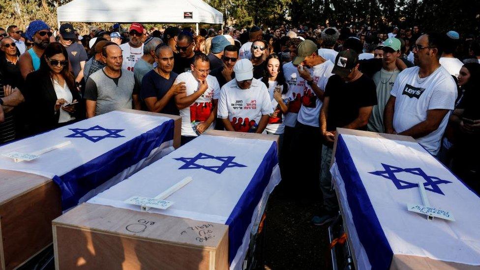 Photo from the funeral of British-Israelis Lianne Sharabi and her daughters, 16-year-old Noiya Sharabi and 13-year-old Yahel Sharabi. People are seen gathered round three coffins with the Israeli flag draped over them