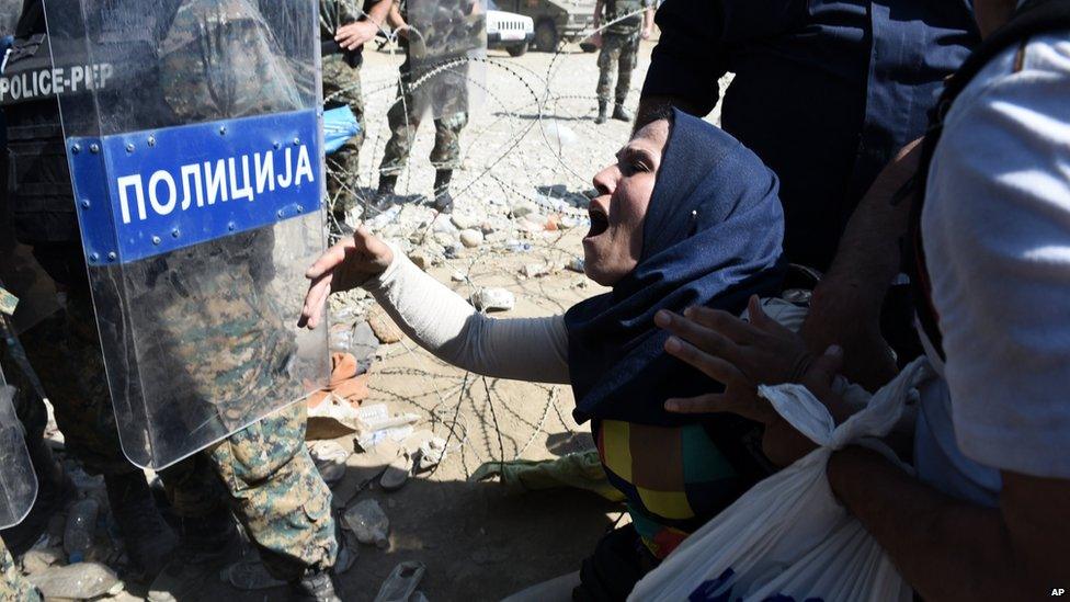 A migrant shouts next to Macedonian policemen as she waits to be allowed to cross the borders from Idomeni town, northern Greece to southern Macedonia, Tuesday, Sept. 1, 2015.