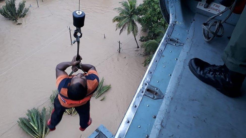 An Indian man being winched up to an Indian Air Force helicopter as he is evacuated from a flood affected area in the southern state of Kerala on 18 August