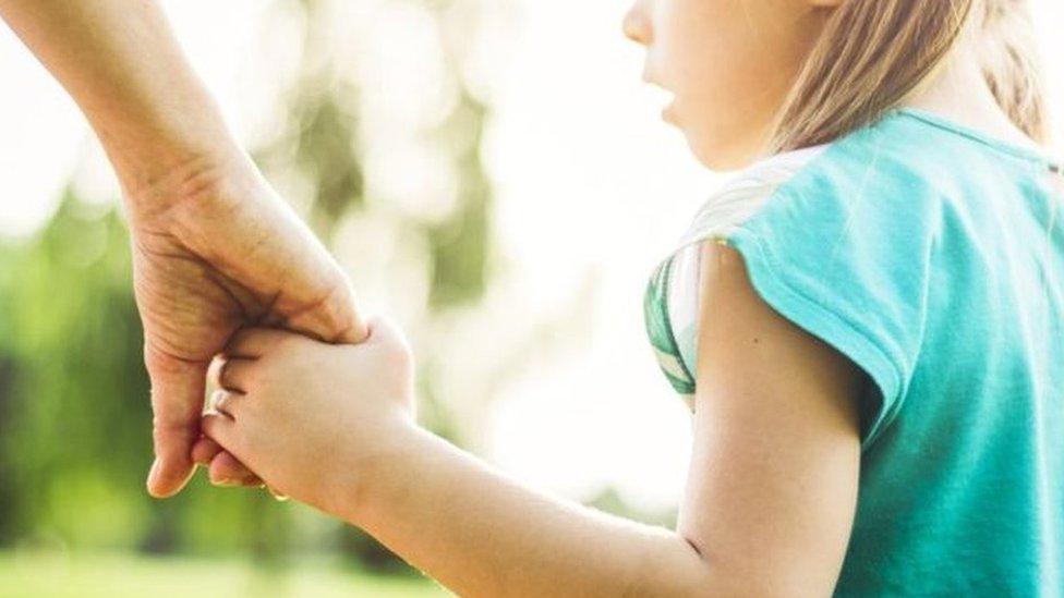 Posed photograph of a child holding hands with an adult