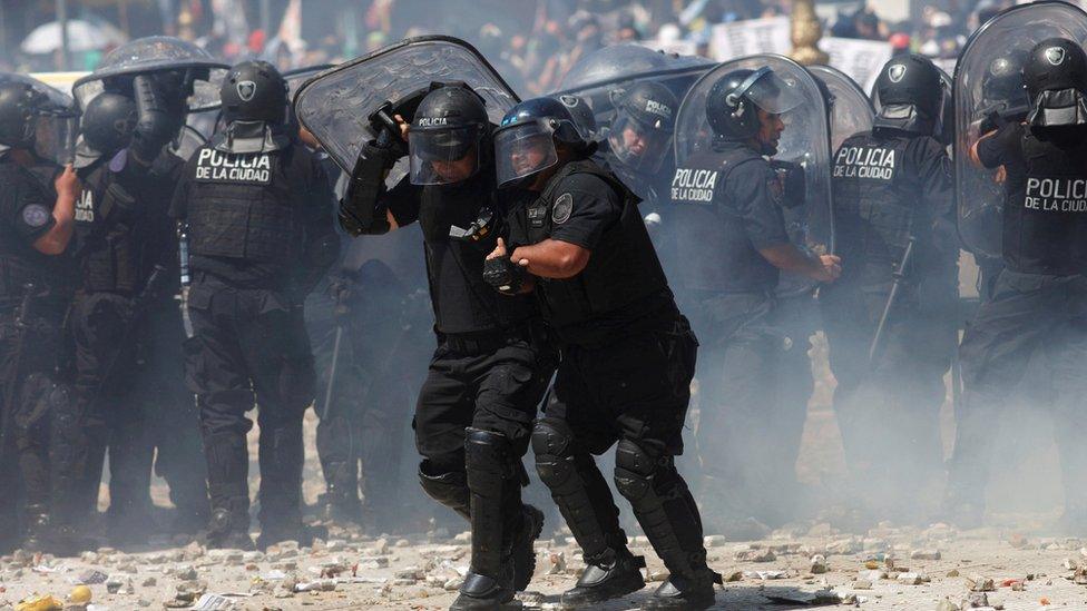 A police officer assists a colleague during clashes with demonstrators as lawmakers debate a pension reform measure, in Buenos Aires