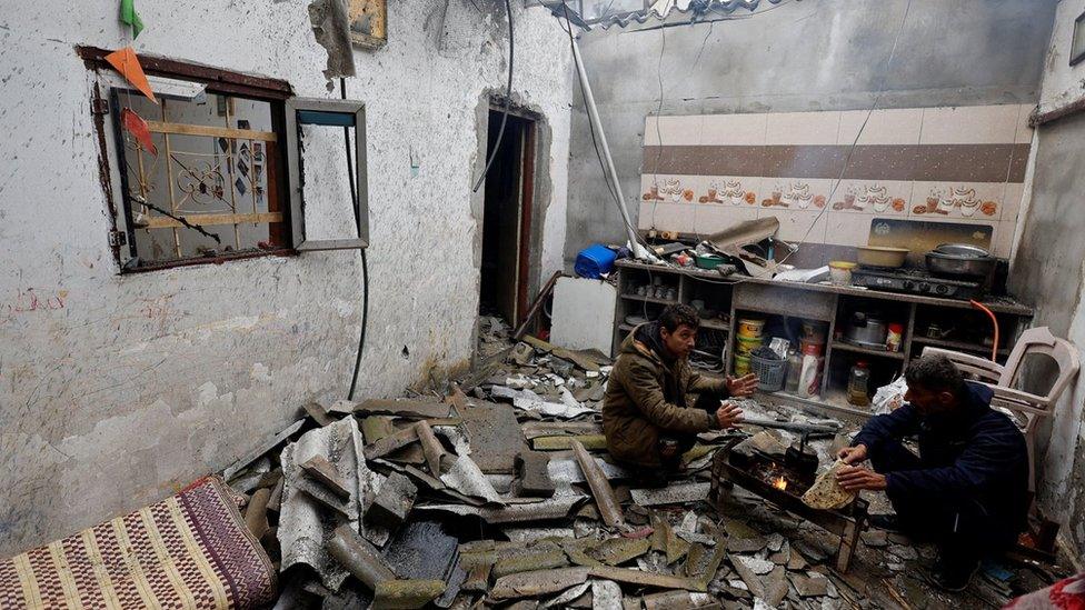 Palestinians crouch next to a fire in a damaged building in Rafah, in the southern Gaza Strip (13 December 2023)