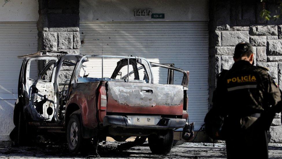 A police officer stands near the remains of a car in Quito, Ecuador