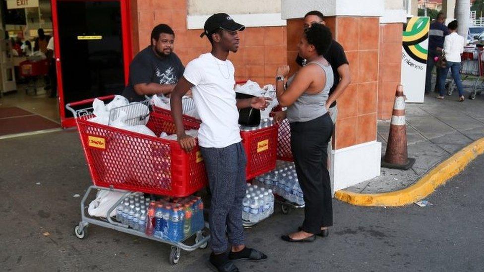 Jamaicans stand next to shopping carts filled with bottled water and other items outside a supermarket in Kingston (30 September 2016)