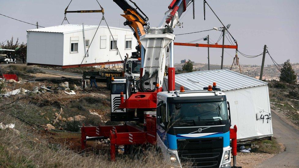 Lorries remove housing units from the unauthorised settlement outpost at Amona