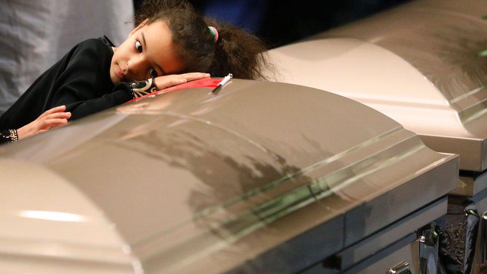 A young mourner lays her head on one of the caskets during funeral services for three of the victims