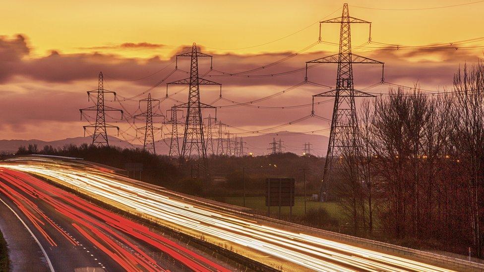 power pilons behind a motorway with clouds in the background