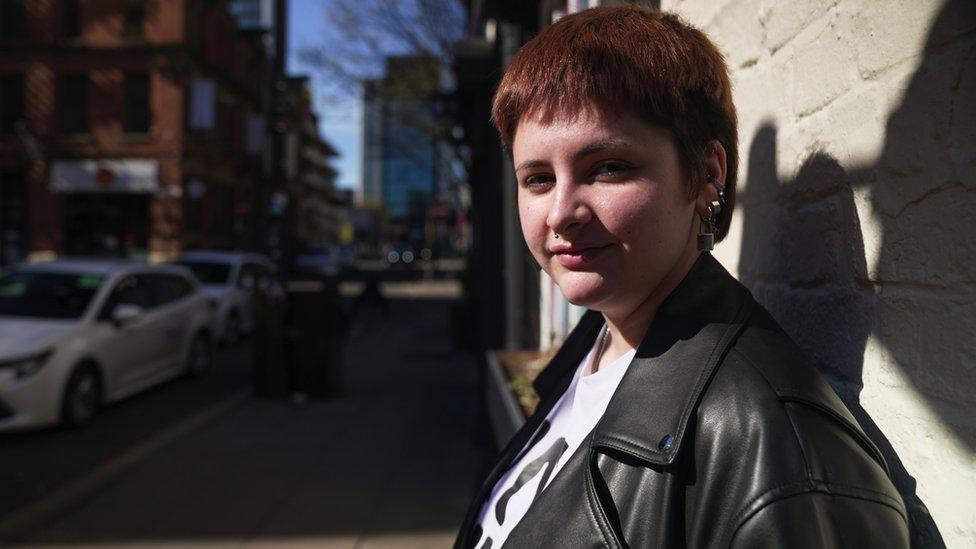 Young person leans against a wall and looks at the camera