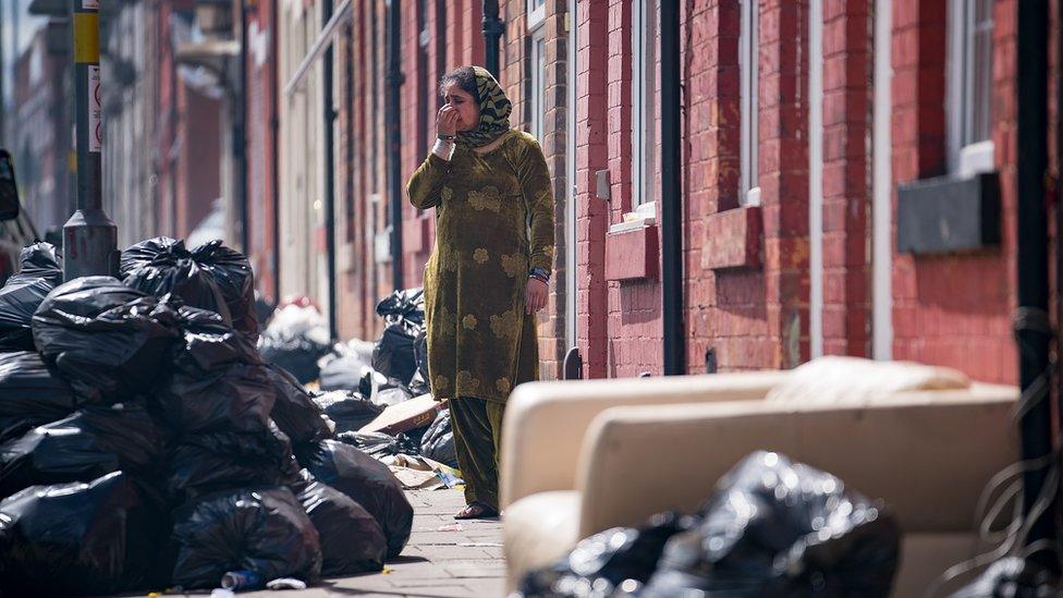 Woman in a street in Alum Rock surrounded by piles of uncollected rubbish bags