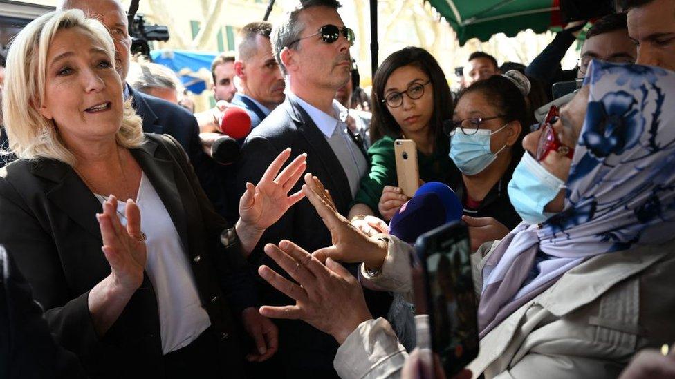 French far-right party Rassemblement National (RN) presidential candidate Marine Le Pen (L) gestures as she speaks with a woman during a campaign visit at Pertuis market on 15 April