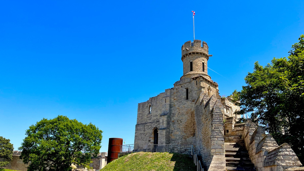 Deep blue skies above Lincoln Castle with green trees in the foreground.