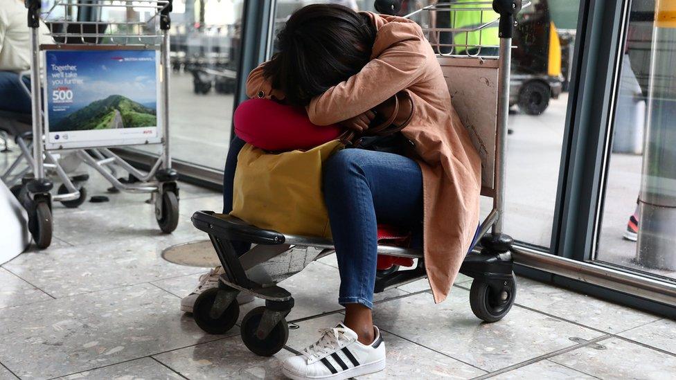 A woman sleeps on a luggage trolley at Heathrow Terminal 5