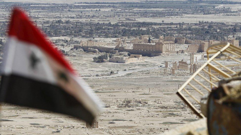 A Syrian national flag flutters as the ruins of the historic city of Palmyra are seen in the background, in Homs Governorate, Syria on 1 April 2016