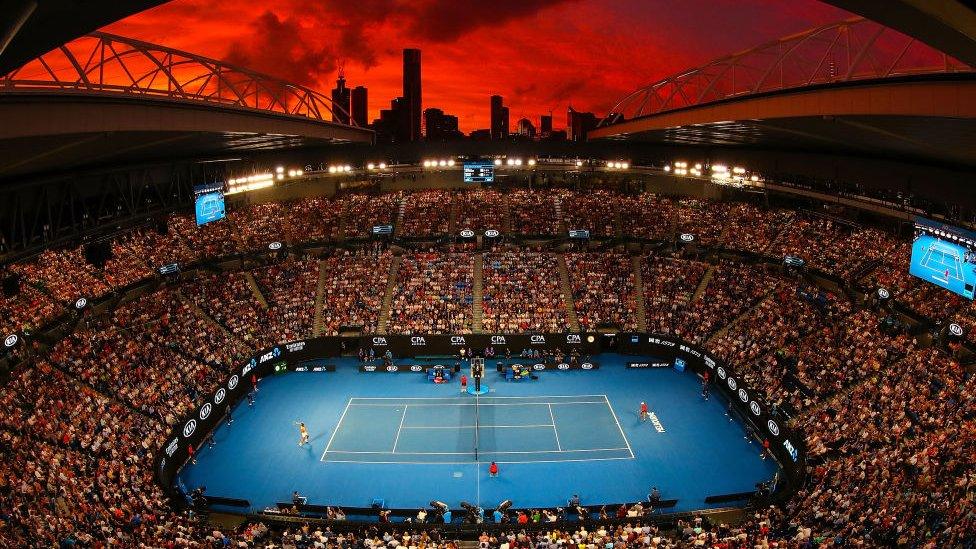 spectators crowded in a massive arena watching a tennis match with the city skyline behind them